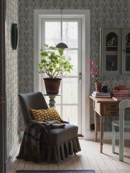 Helle Inneneinrichtung mit Sessel, Tisch, Pflanze und floraler Tapete für ein gemütliches Ambiente.