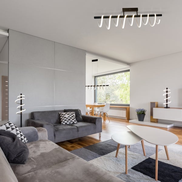 Wohnzimmer mit grauer Couch, Teppich, Couchtischen und moderner Beleuchtung.