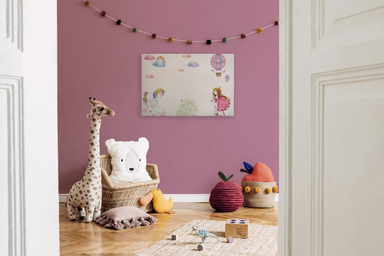 Ein Kinderzimmer mit einem Wandbild, das ein Einhorn und eine Prinzessin zeigt, umgeben von Plüschtieren, Dekoration und einem Holzspielzeug.