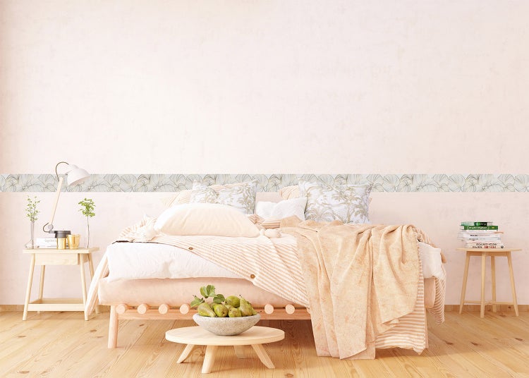 Helles Schlafzimmer mit Holzbett, gemusterten Kissen und einer dekorativen Tapetenbordüre mit Blattmotiv an der Wand.