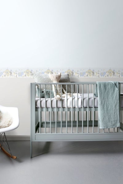 Kinderzimmer mit Gitterbett, Spielzeug und Zirkus-Bordüre an der Wand.