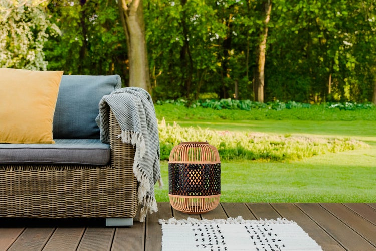 Szene im Garten mit Rattansofa, Kissen, Decke, Teppich und Laterne