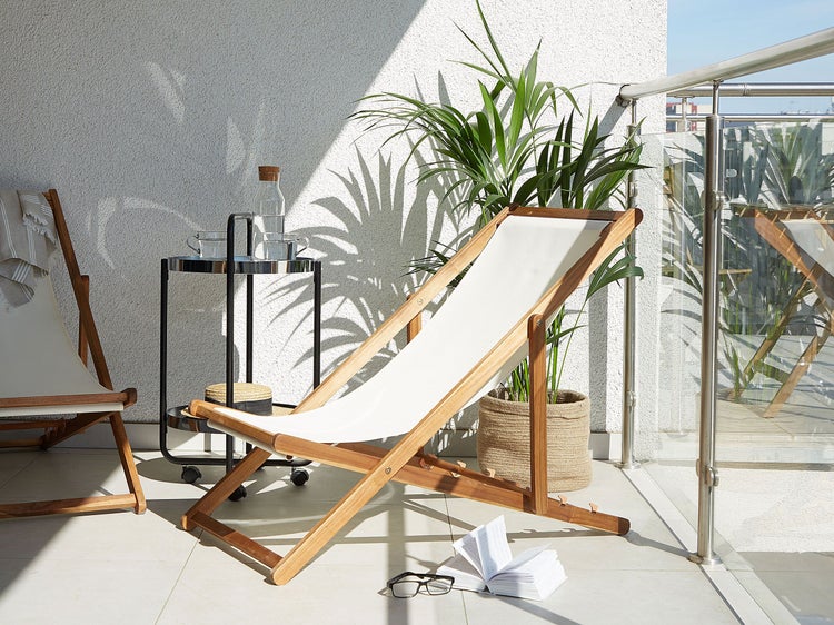 Szene auf einem Balkon mit zwei Holzliegestühlen, einem Beistelltisch, einer Pflanze und einem Buch