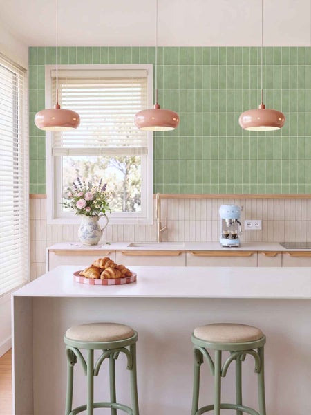 Moderne Küche mit Fliesenwand im Hochformat, Kochinsel mit zwei Hockern, Pendelleuchten und Küchenzeile mit Arbeitsplatte sowie Blumenstrauß.