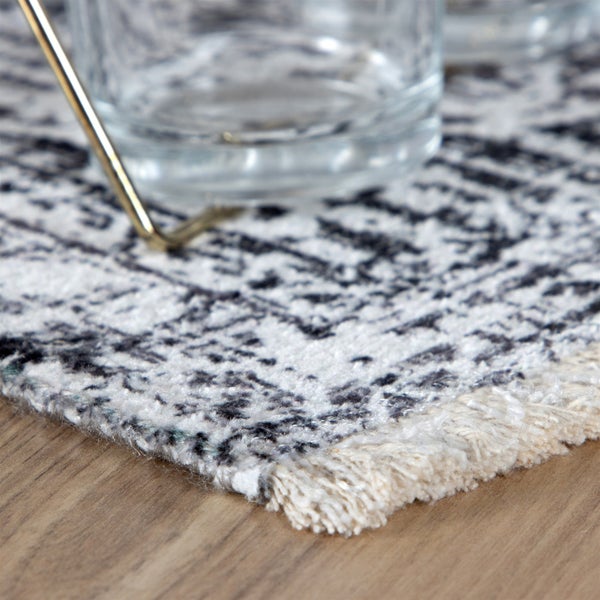 Detailansicht eines gemusterten Teppichs mit Fransen auf einem Holzboden.