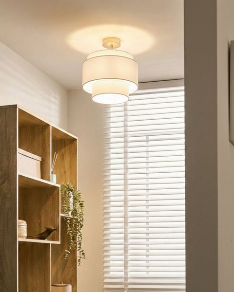 Moderne Deckenleuchte mit dreistufigem Textilschirm in einem hellen Raum mit Holzregal und Jalousien.