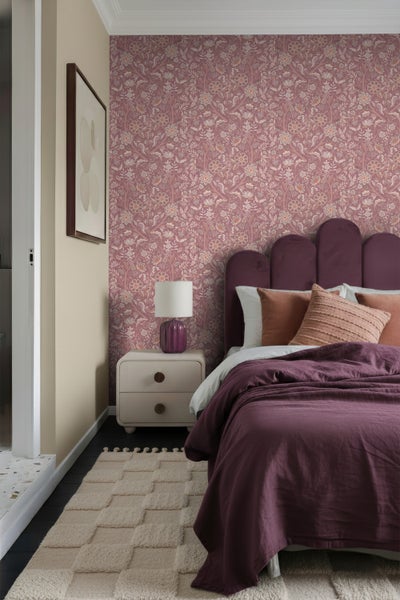 Schlafzimmer mit gemusterter Tapete, Bett, Nachttisch, Lampe und Teppich