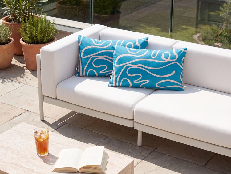 Zwei rechteckige Outdoor Kissen mit wellenförmigem Linienmuster auf einer weißen Gartenbank auf einer Terrasse.