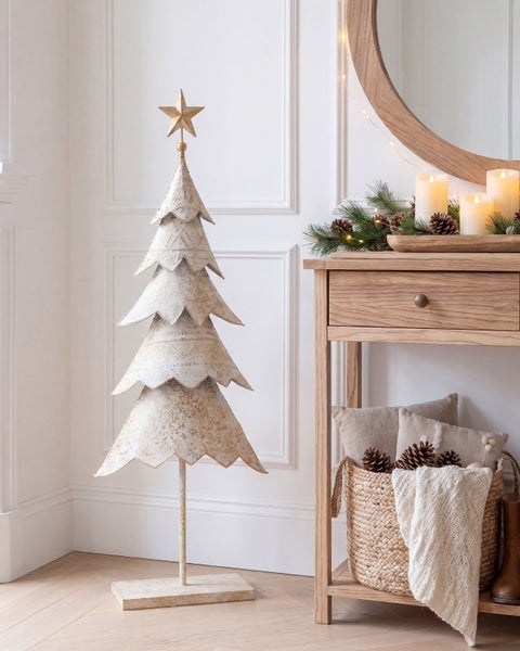 Dekorativer Weihnachtsbaum aus Metall im Vintage Stil neben einem Holztisch mit Kerzen und Korb.