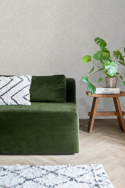 Nahaufnahme eines Wohnzimmers mit grünem Sofa, Holzhocker, Zimmerpflanze und gemusterter Tapete