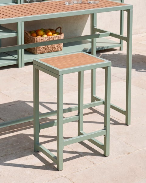 Barhocker mit grünem Metallgestell und Sitzfläche aus Holzlamellen vor einem passenden Bartisch auf einer Terrasse.