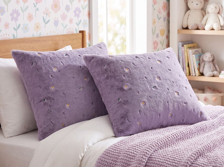 Zwei flauschige Zierkissen mit gesticktem Blumenmuster auf einem Kinderbett im gemütlichen Kinderzimmer.