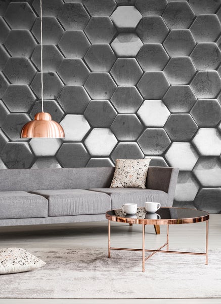 Fototapete mit 3D-Wabenmuster in Betonoptik, modernes Wohnzimmer mit grauem Sofa, kupferfarbenem Couchtisch und Hängelampe.