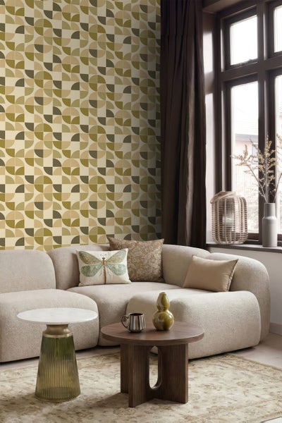 Vliestapete mit grünem und beigem geometrischem Muster in einem modernen Wohnzimmer mit hellem Sofa, Holztisch und Dekoration.