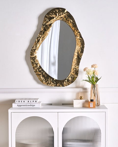 Dekoratives Interieur mit Spiegel mit goldenem Rahmen über einem weißen Schrank
