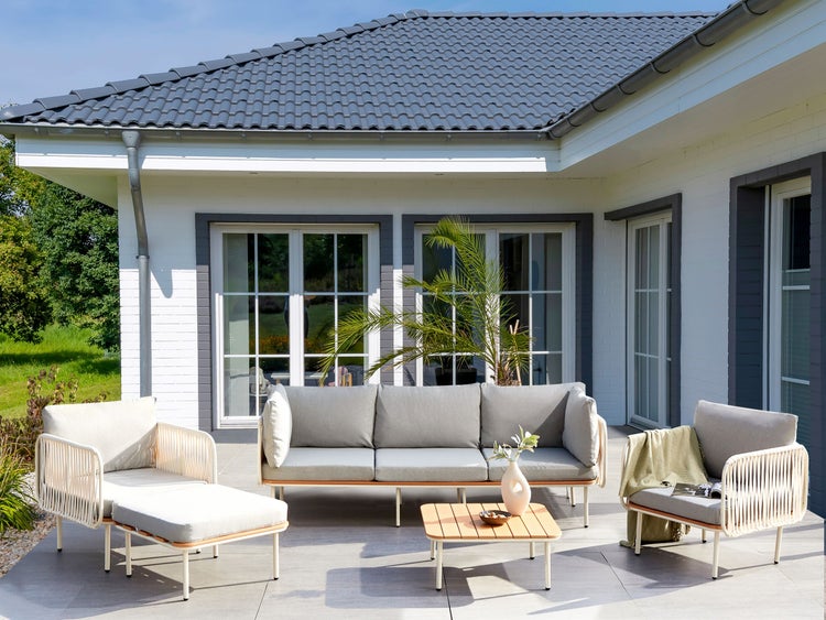 Terrasse mit Sitzgruppe bestehend aus Sofa, Sessel und Tisch vor einem Wohnhaus.
