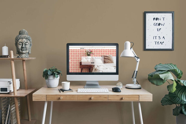 Aufgeräumtes Homeoffice mit hellem Holzschreibtisch, Monitor, weißer Schreibtischlampe, Buddha-Statue und Zimmerpflanzen in einem modernen Raum.