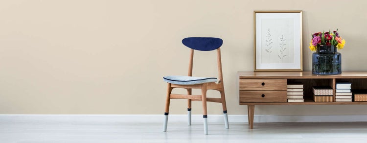 Modernes Wohnzimmer mit Holzstuhl mit blauem Polster neben einem Sideboard aus Holz mit Schubladen, gerahmtem Bild und Blumenvase.