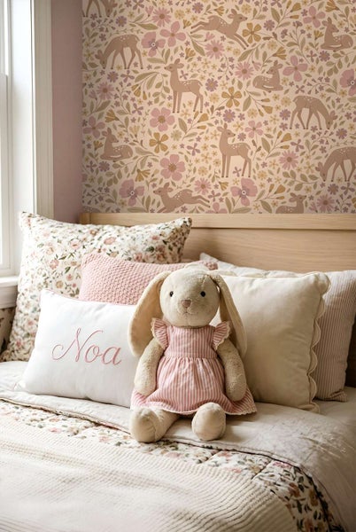 Kinderzimmer mit Blumentapete mit Rehmotiv, helles Holzbett mit Stofftieren und dekorativen Kissen im floralen und gestreiften Design.