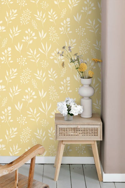 Tapete mit weißem Blattmuster auf gelbem Hintergrund, hölzerner Beistelltisch mit Blumenvasen und Schublade mit Geflecht.