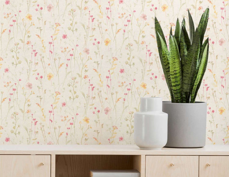 Tapete mit dezentem Wiesenblumenmuster auf hellem Grund, kombiniert mit einer Pflanze in einem grauen Übertopf auf einem hellen Holzregal.
