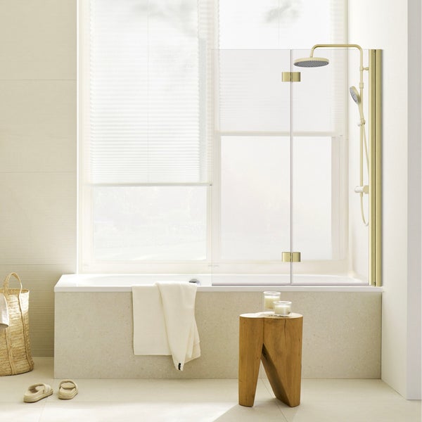 Badewanne mit gläserner Duschabtrennung und Duschsystem in Gold in einem hellen, modernen Badezimmer.