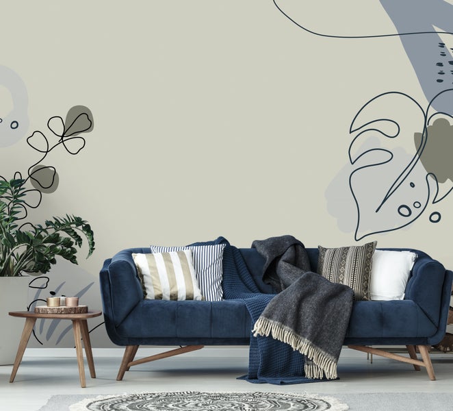 Wohnzimmer mit abstrakter Fototapete mit Pflanzenmotiven, einem blauen Samtsofa mit Kissen und einem runden Beistelltisch aus Holz.