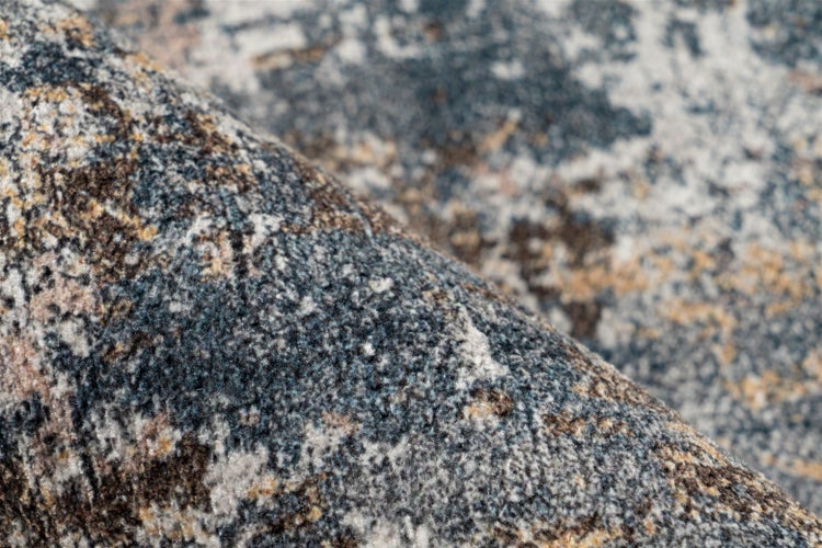 Nahaufnahme eines Kurzflorteppichs mit abstraktem Muster in Blau, Grau und Braun.