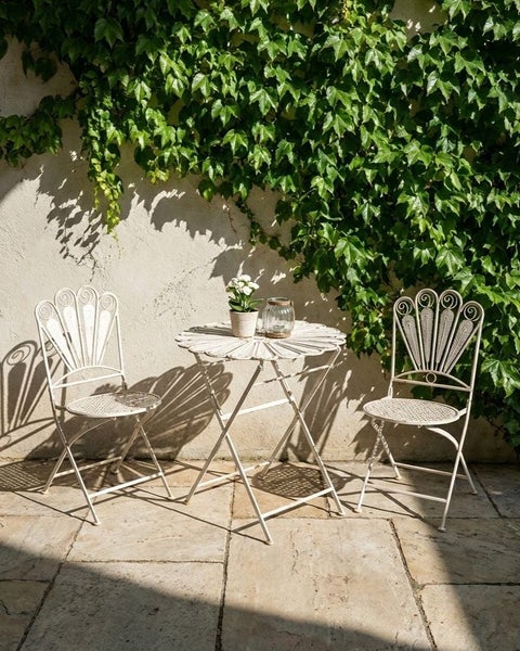 Gartenszene mit Tisch und zwei Stühlen aus Metall vor einer mit Efeu bewachsenen Wand