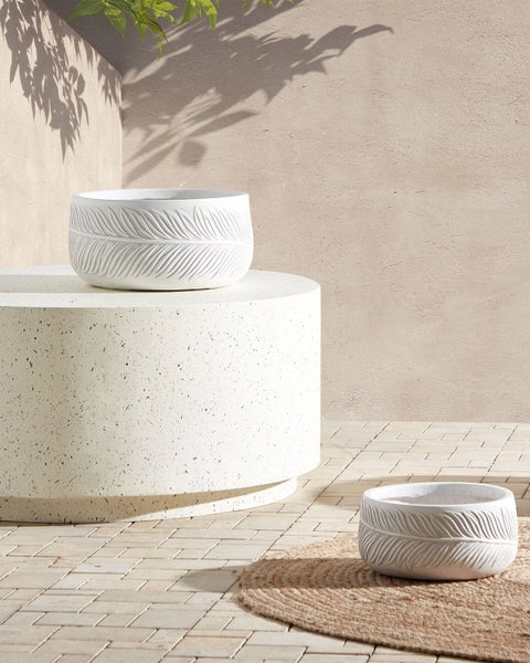 Zwei weiße Pflanzgefäße mit Federmuster in einer Gartenszene.