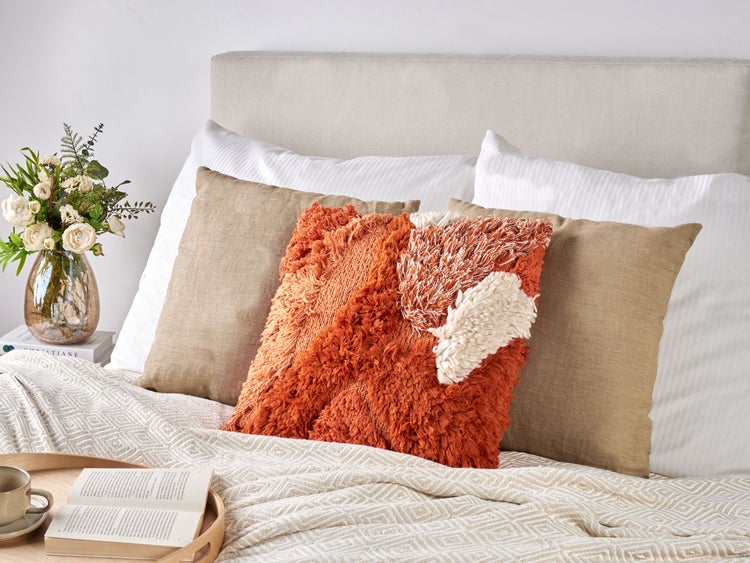 Gemütliches Schlafzimmer mit Kissen, Decke, Blumen und Buch auf dem Bett