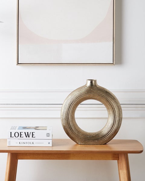 Dekorative goldfarbene Vase in Ringform auf einem Holztisch
