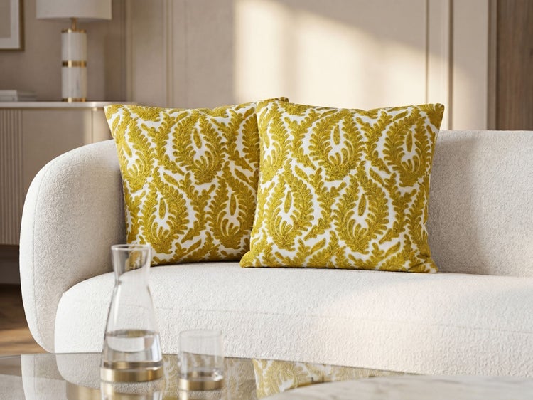 Zwei quadratische Zierkissen mit gelber Stickerei auf einem weißen Sofa in einem hellen Wohnzimmer.