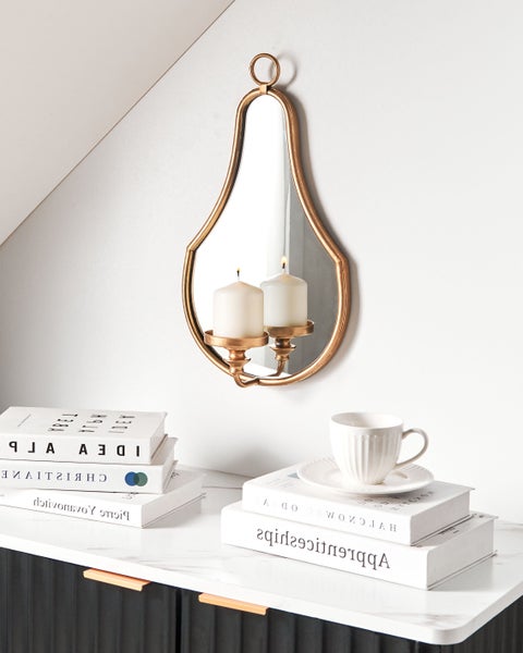 Dekoratives Stillleben mit Kerzen, Spiegel, Büchern und Tasse auf einem Schrank