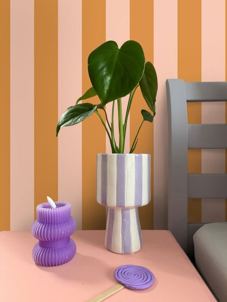Dekorative Szene mit einer Zimmerpflanze in einem gestreiften Topf, einer spiralförmigen Kerze und einem Lolli auf einem Tisch