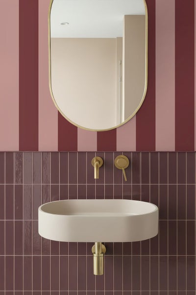 Modernes, ovales Waschbecken an einer Wand mit vertikalen Fliesen und gestreifter Tapete, mit passenden Wandarmaturen und einem ovalen Spiegel.