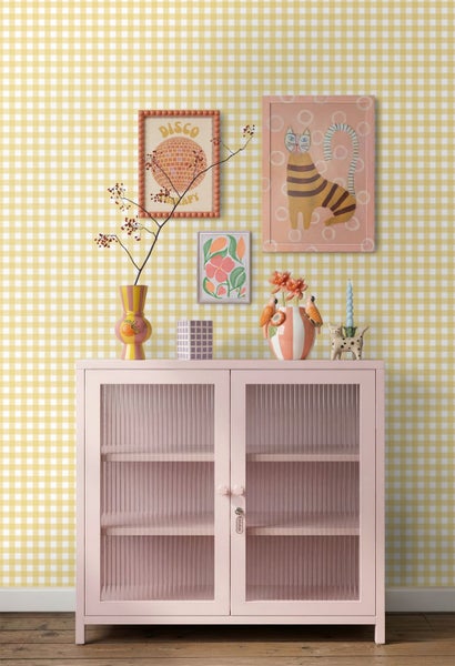 Innenraum mit gelb-weiß karierter Tapete hinter einer rosa Vitrine mit geriffeltem Glas, dekoriert mit bunten Vasen und eingerahmten Wandbildern.