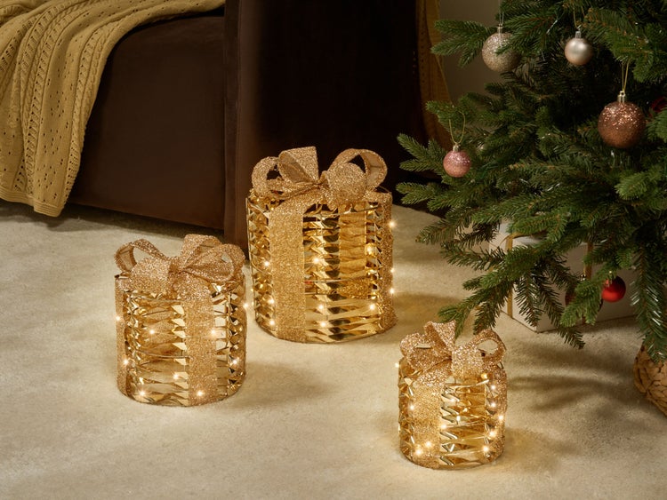 Dekorative goldfarbene Geschenkpakete mit Beleuchtung neben einem Weihnachtsbaum und einem Sofa.