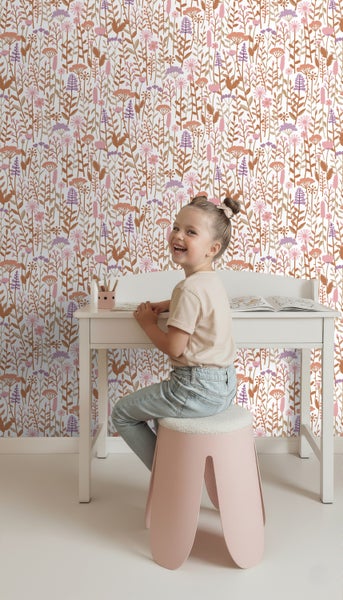 Ein Mädchen sitzt an einem Schreibtisch vor einer Wand mit Blumentapete.