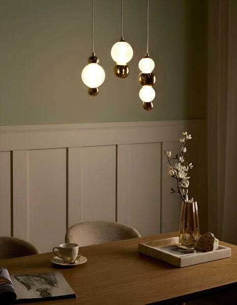 Szene mit Esstisch, Stühlen und drei Pendelleuchten mit kugelförmigen Lampenschirmen.