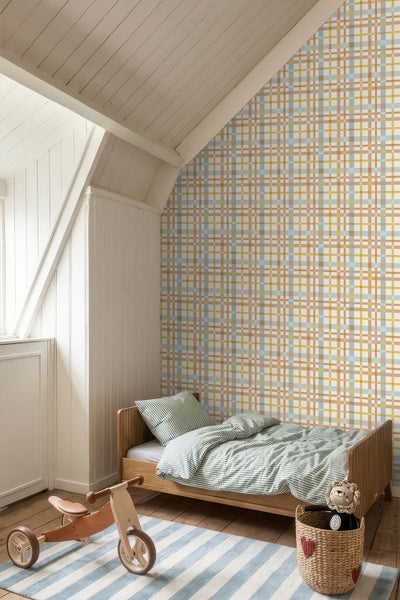 Tapete mit buntem Karomuster in einem hellen Kinderzimmer mit Dachschräge, Holzbett und gestreifter Bettwäsche.