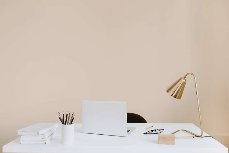 Moderner, organisierter Arbeitsplatz mit weißem Schreibtisch, Laptop, goldener Schreibtischlampe und Schreibutensilien.