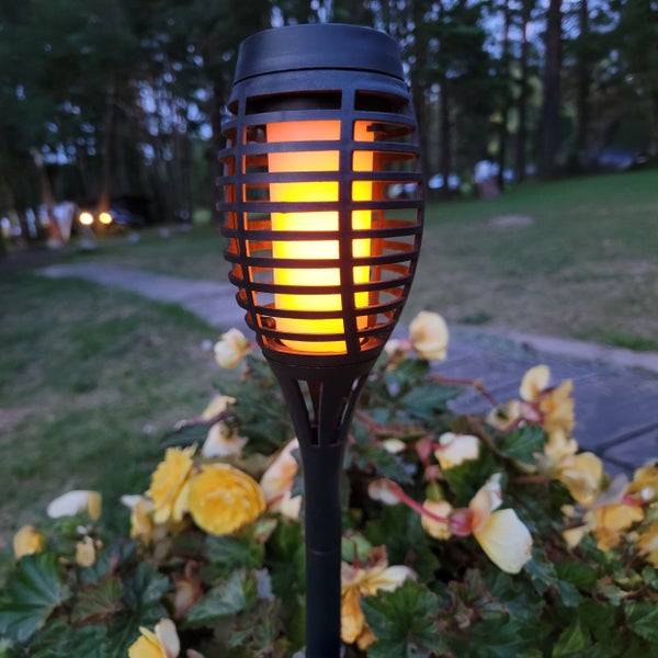 Gartenfackel mit Flammeneffekt zwischen Blumenbeet