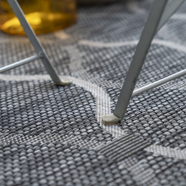 Detailansicht von Metalltischbeinen mit Kunststoffgleitern auf einem gewebten Outdoor-Teppich mit Muster.