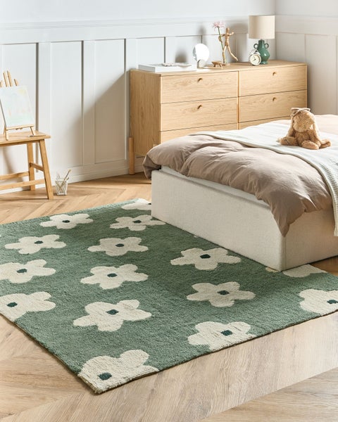 Grüner Teppich mit weißem Blumenmuster in einem hellen Kinderzimmer mit Holzmöbeln und Parkettboden.