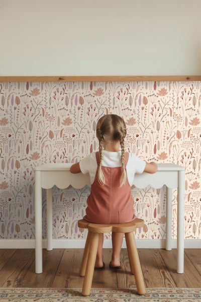 Mädchen sitzt an einem weißen Schreibtisch vor einer Wandtapete mit floralem Muster.