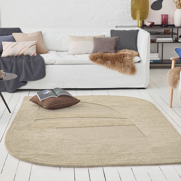 Moderner Wohnraum mit beigefarbenem strukturiertem Teppich mit geometrischem Muster auf weißem Holzboden vor einem weißen Sofa mit Kissen.