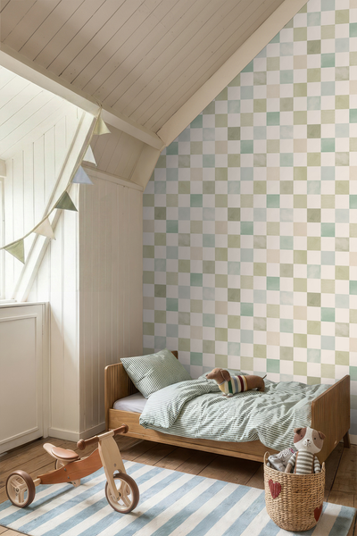 Kinderzimmer mit karierter Tapete, einem Holzbett mit gestreifter Bettwäsche und einem Holzdreirad auf einem gestreiften Teppich.