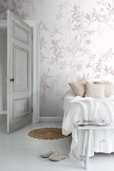 Helles Schlafzimmer mit Blumentapete, geöffneter Tür und Strickdecke