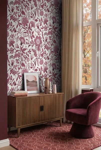 Wohnzimmer mit floral gemusterter Tapete, einem Sideboard aus Holz mit Rillenstruktur, einem Sessel aus Samt und einem gemusterten Teppich.